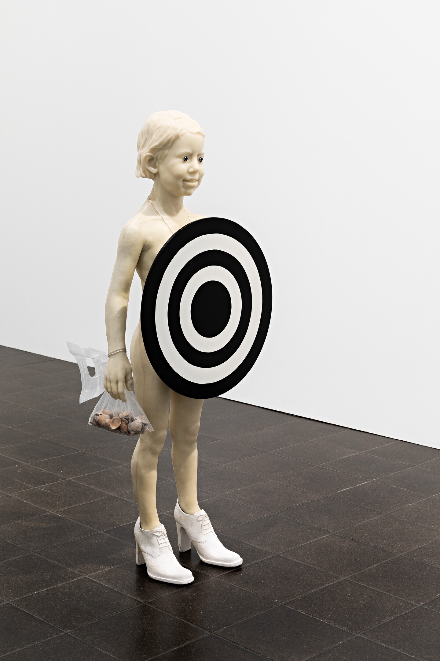 Skulptur: Frau in weißem Kleid hält große schwarz-weiße Zielscheibe in Galerie