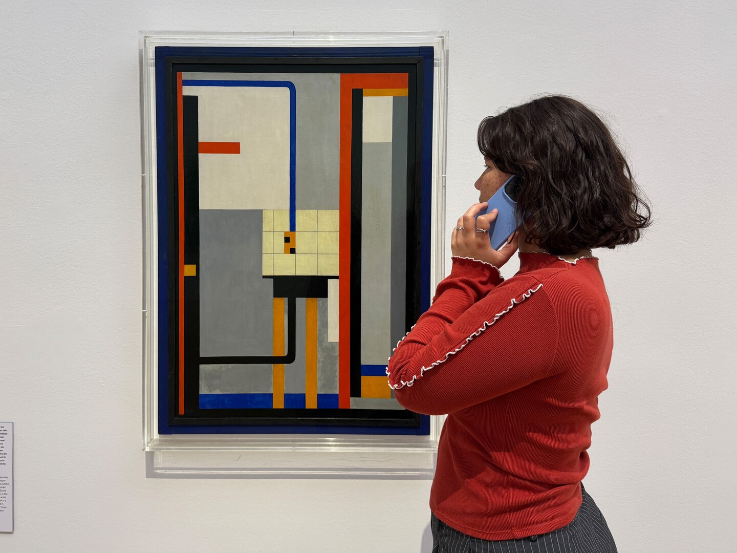 Frau in rotem Pullover betrachtet abstraktes Gemälde mit geometrischen Formen in der Ausstellung »This Is the Modern World«