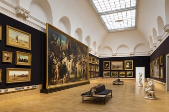 Großer Museumsraum mit dunklen Wänden, historischen Gemälden, Sitzbänken und Oberlicht
