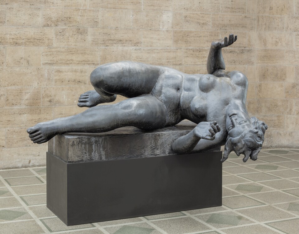 Bronzeskulptur einer liegenden Figur in abwehrender Haltung auf schwarzem Sockel