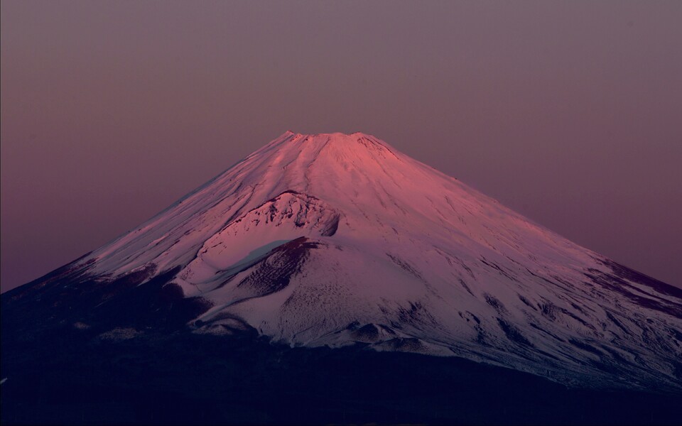 Schneebedeckter Vulkangipfel in rosa Abendlicht vor violettem Himmel