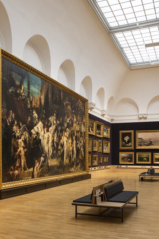 Großer Museumsraum mit dunklen Wänden, historischen Gemälden, Sitzbänken und Oberlicht