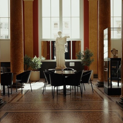 Blick in eleganten Säulenraum mit hohen Decken, Tischen, Stühlen und einer Skulptur